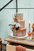 Hochzeitstorte in Kupfertönen mit Blumendekor auf festlich gedeckter Kommode