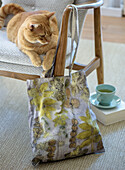 Fabric bag with leaf pattern and cat on grey armchair