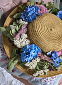 Straw hat with blue hydrangeas (Hydrangea) and white yarrow (Achillea)