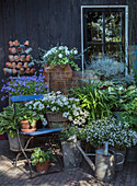 Blumenarrangement und dekorative Metallobjekte vor Holzwand im Garten