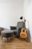 Grauer Sessel mit Hocker und Gitarre in Zimmerecke