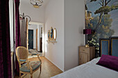 Schlafzimmer mit Wandgemälde und barockem Rattanstuhl