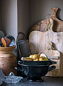 Kitchen corner with wooden utensils, black colander and fresh fruit