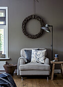 Light grey armchair with cushions in front of dark grey wall with rustic wreath