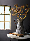 Dried flowers in a metal pot on a round side table in front of a window