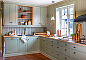 Classic country-style kitchen in mint green with wooden worktops and hanging lamps