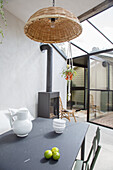 Conservatory with glass roof, black dining table and wicker lamp