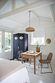 Light-flooded bedroom with dining table, rat chairs and black wardrobe