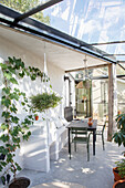 Conservatory with hanging plants, bench, table and metal chairs