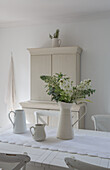 White country-style dining room with table decoration of milk jugs and bouquet of flowers