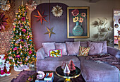 Living room with festively decorated Christmas tree and velvet sofa in light purple