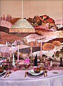 Dining table set with colourful landscape wallpaper and pink candles