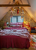 Bedroom under the roof with bed, wooden beams and paper poinsettias