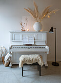 White piano with sheet music, vase with pampas grass and fairy lights