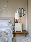 Bedroom with light-coloured bed, rustic bedside table and round mirror