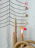 Three candles in a curved candle holder in front of an embroidered fabric background