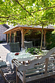 Wooden seating area in the sunny garden under a pergola with vines