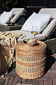 White wine and snacks on woven rattan stool next to sun loungers in the garden