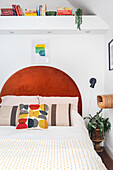 Bed headboard in brick red and bed with patterned cushions in bedroom