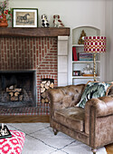 Brown leather armchair in front of brick fireplace with wood pile