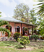 Pink house with wooden veranda and tropical plants in the garden