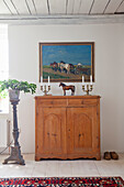 Wooden chest of drawers with candlesticks and horse statue in front of farmhouse painting