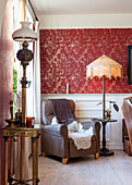 Armchair with fur and side table with floor lamp in front of red, patterned wallpaper