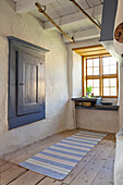 Rustic hallway with wooden floor, blue wall cupboard and striped carpet runner