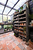 Spacious greenhouse with terracotta floor tiles and shelf full of clay pots