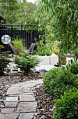 Garden path made of stone slabs leads to a modern seating area with privacy screen and plenty of greenery