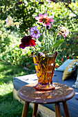 Colourful summer flowers in an amber-coloured vase on a wooden chair in the garden