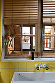 Wooden window with louvre blinds in the bathroom with yellow tiles