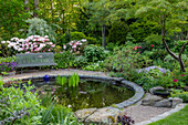 Garten mit rundem Teich, Sitzbank und blühenden Rhododendren