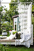 Sun bed with crocheted curtain and cushions in the garden