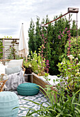 Roof terrace with raised bed and seating area made of rattan and knitted poufs