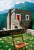 Stone house with red door and garden chair against a mountain backdrop