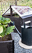 Black raised bed with mini greenhouse and watering can in the garden