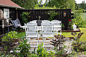 White garden furniture on paved terrace in front of black wooden fence and green landscape