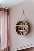 Round wall shelf with doll figures on pink wall in children's room