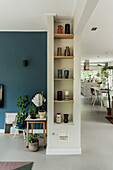 Living room with blue accent wall, shelf with vases and open kitchen