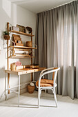 Wooden desk with shelf and basket decoration in front of floor-length curtains in the study