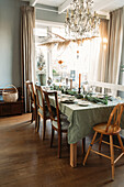 Dining table set with a green tablecloth and wooden furniture under a chandelier