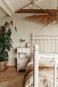 Bedroom with white metal bed, bedside table and houseplant on wooden floor