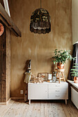 White chest of drawers with houseplant and retro hanging lamp against a beige-brown wall