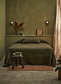 Bedroom with olive green wall colour, bedspread and wooden stool