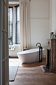 Freestanding bathtub in front of bay window with wooden blinds in elegant bathroom