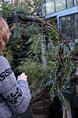 Woman makes door wreath from fir branches, juniper, eucalyptus and a string of lights