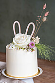 White cake with floral decorations and paper bunny ears