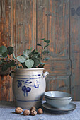 Kölner Topf mit Eukalyptuszweigen und Geschirr vor Holzverkleidung