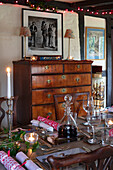 Festively laid dining table in front of antique chest of drawers and framed photography